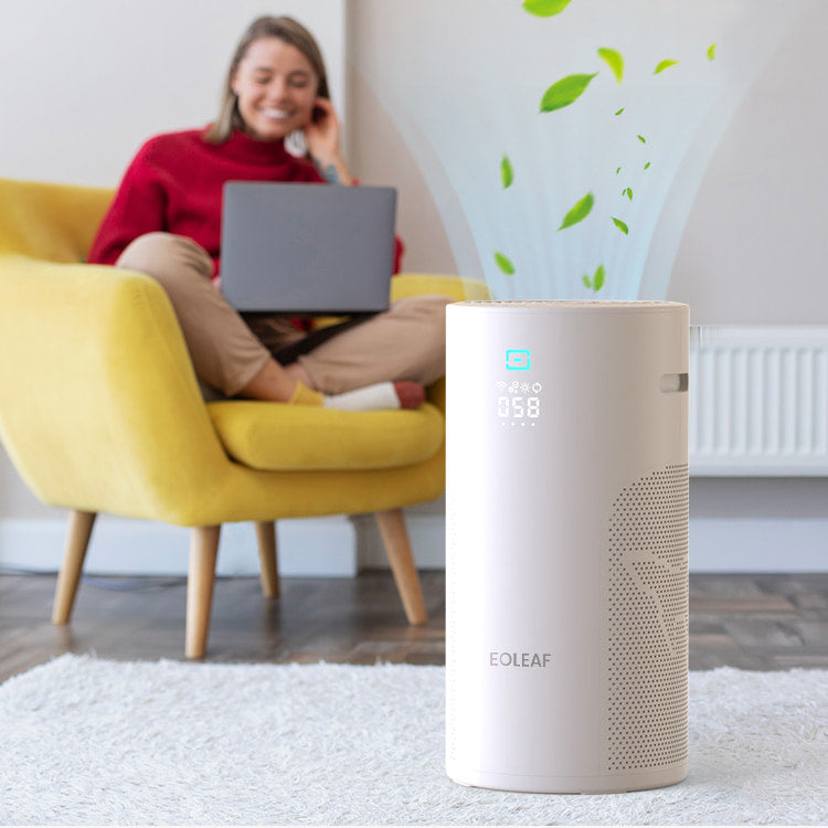 A woman sitting in a chair on her laptop next to Eoleaf's AEROPRO 40 air purifier